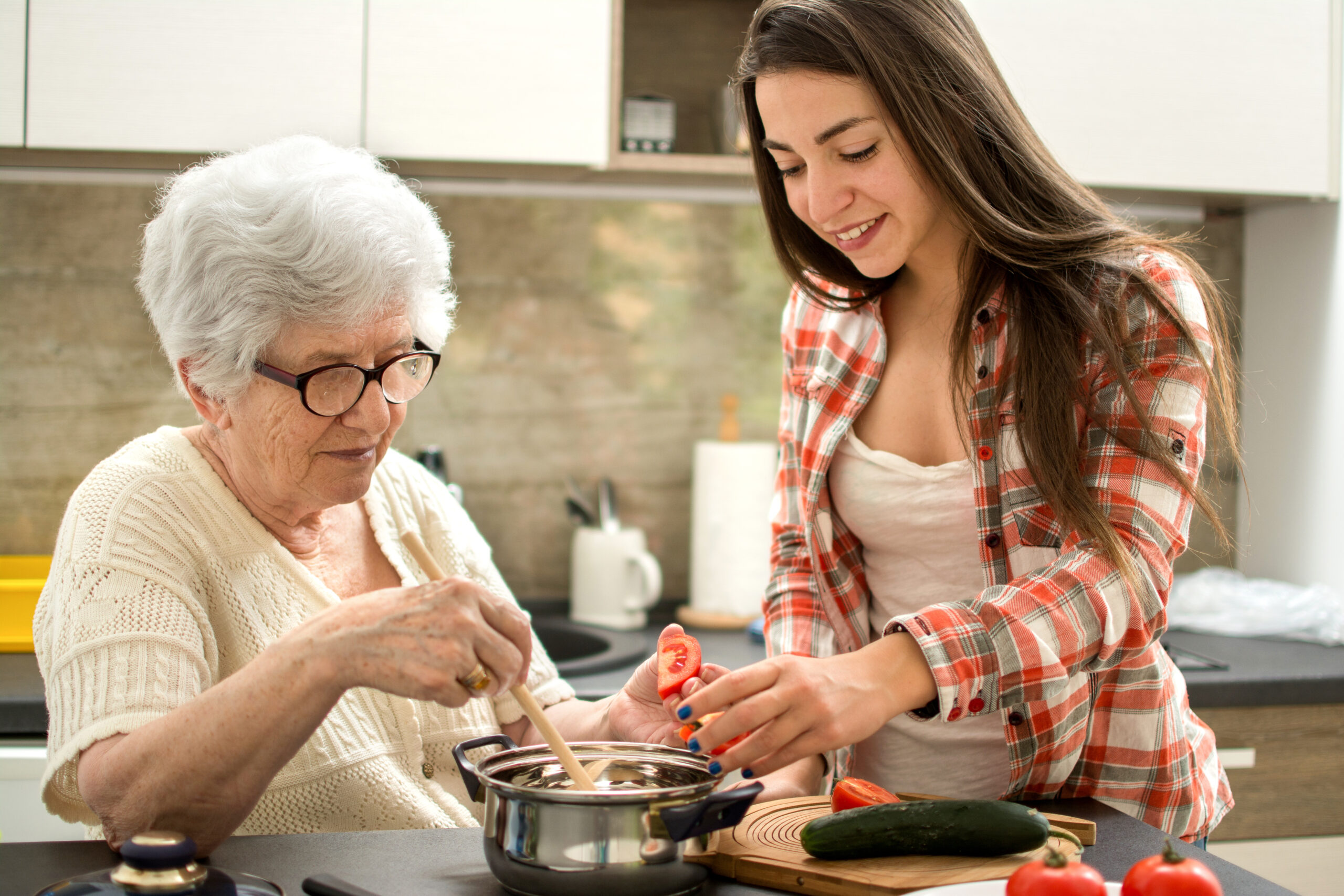 Senior woman cooking with her granddaughter in a modern kitchen — preparing healthy meals together as part of balanced senior nutrition and caregiving at home.