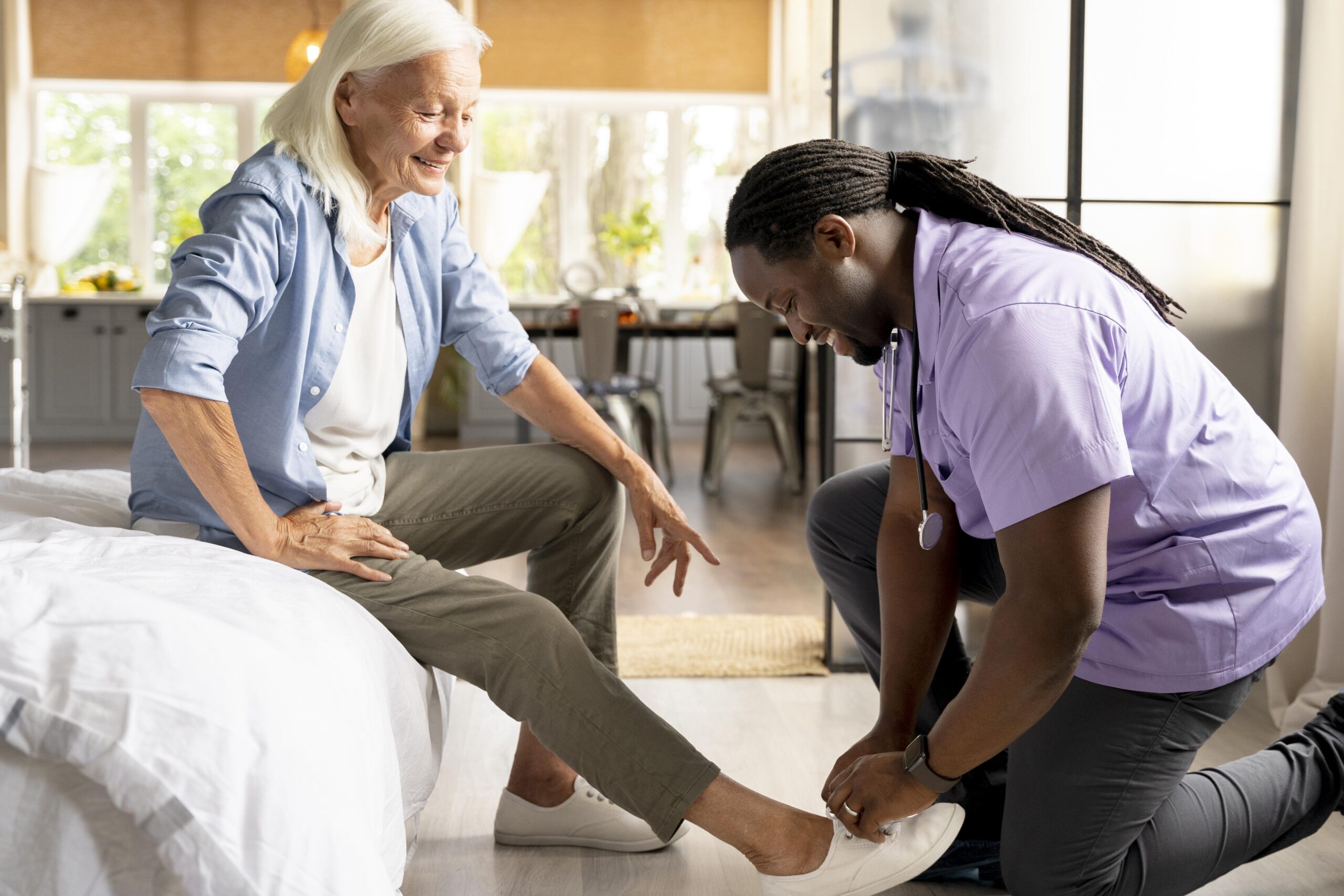 Caregiver assisting a senior woman with putting on shoes at home in Brookline
